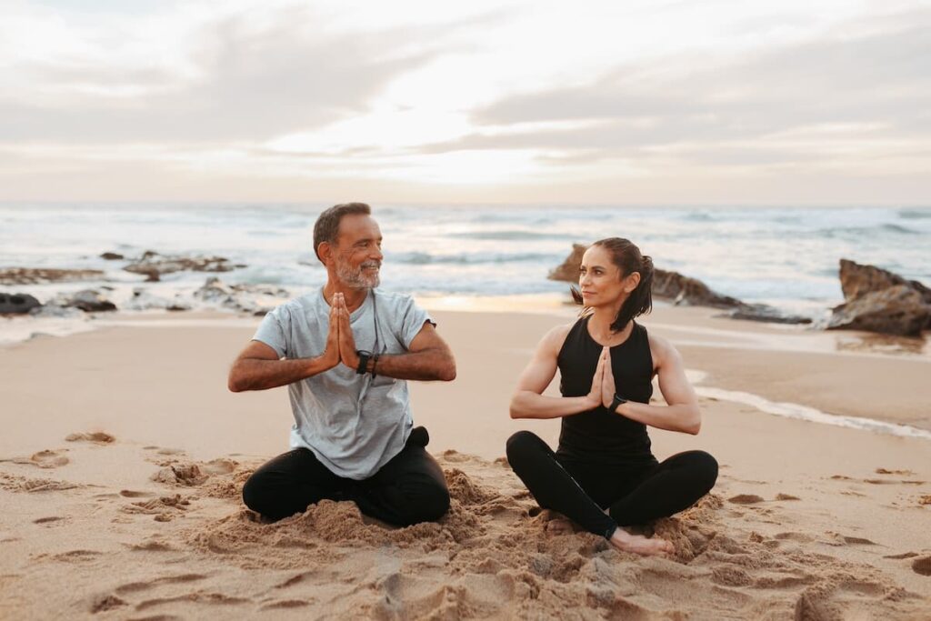Man and woman doing yoga on a sandy beach