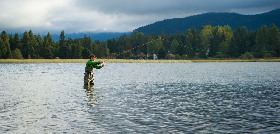 Man Fishing in Whistler in Spring surrounded by green trees and mountains