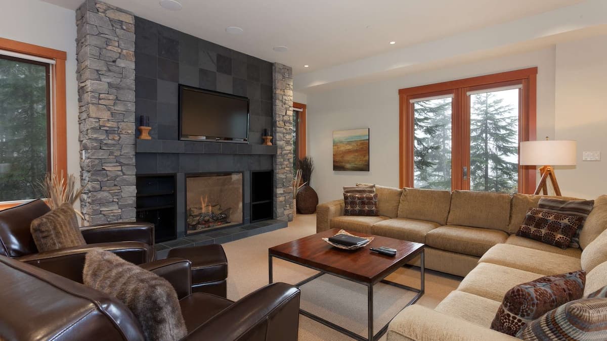 Media room with black stone fireplace with TV mounted above it and a large beige couch with two dark leather arm chairs beside it