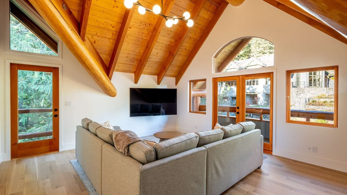 Media room with grey L shaped couch and tall wooden ceilings with TV mounted onto the wall