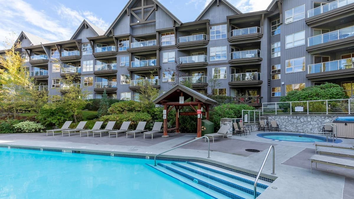 Exterior of aspens building with balconies overlooking pool and hot tub with sun beds next to the pool