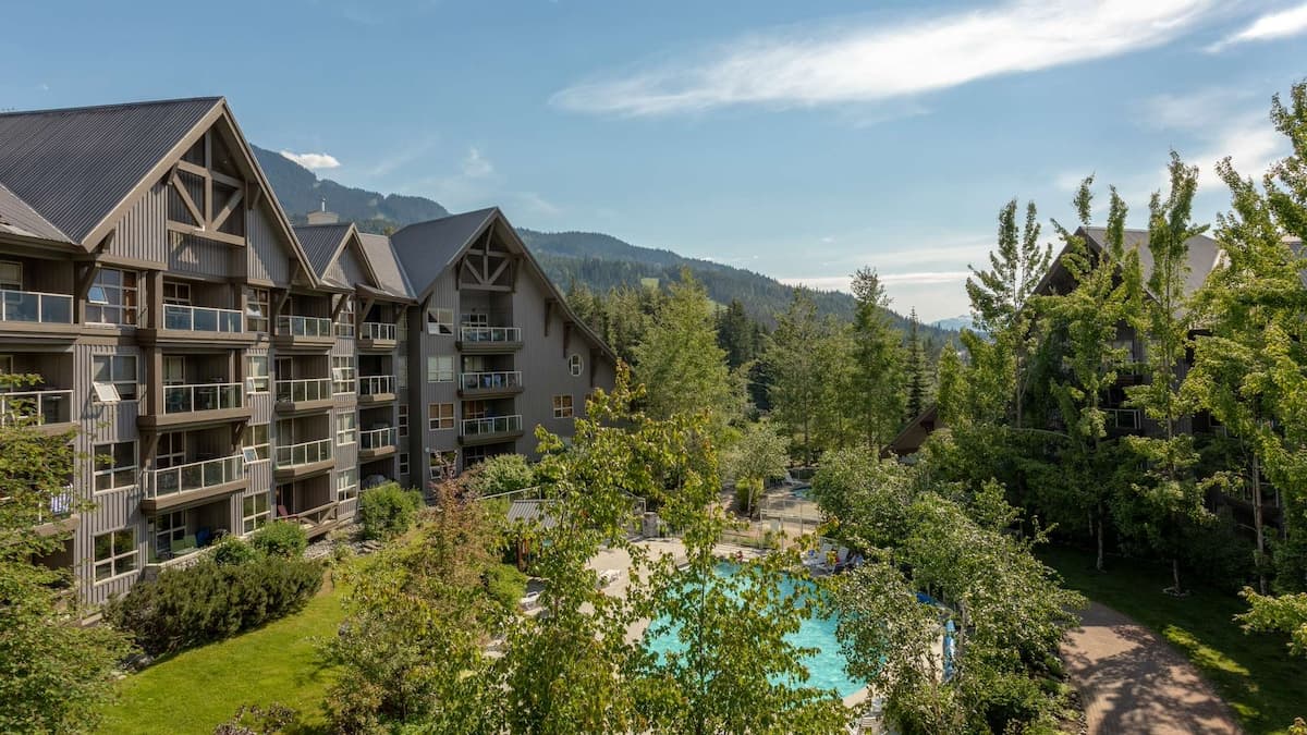 View of the Aspens building with pool under the trees and mountain views and blue skies in background