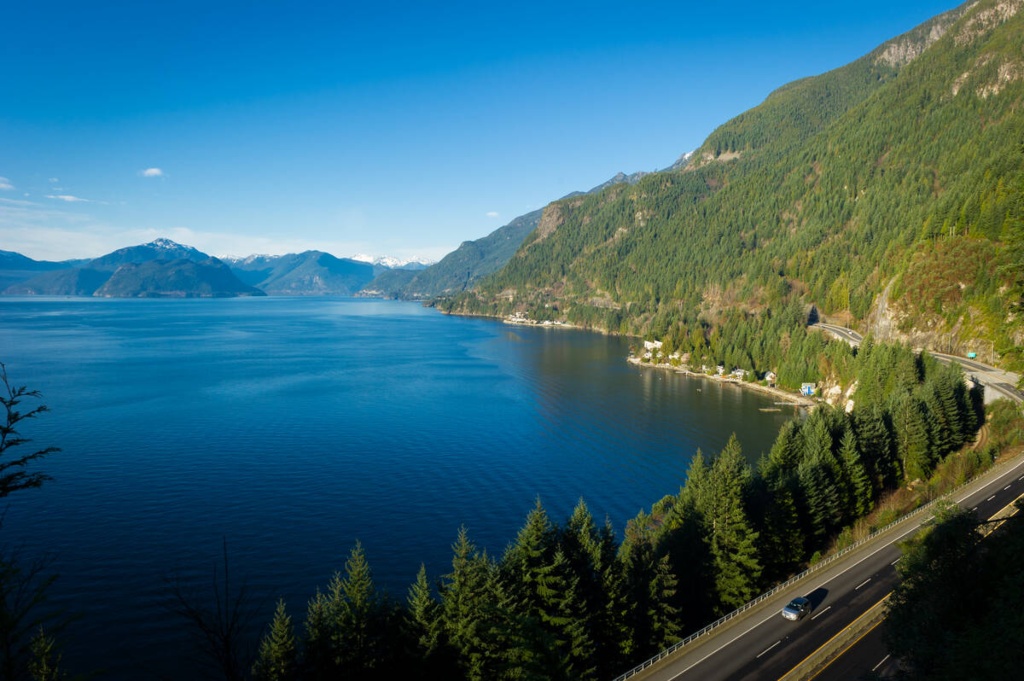 Scenic drive along the Sea to Sky Highway from Vancouver to Whistler, with ocean views, forested mountains, and a clear blue sky.