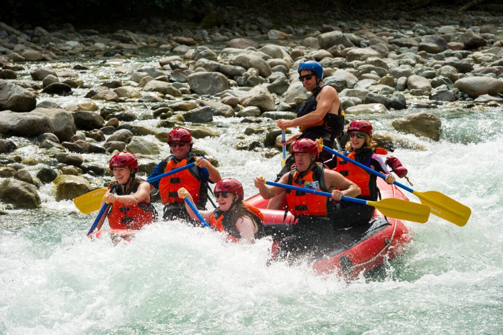 Adventurers white-water rafting down a rushing river near Whistler, BC, paddling together through thrilling rapids surrounded by rugged natural beauty.